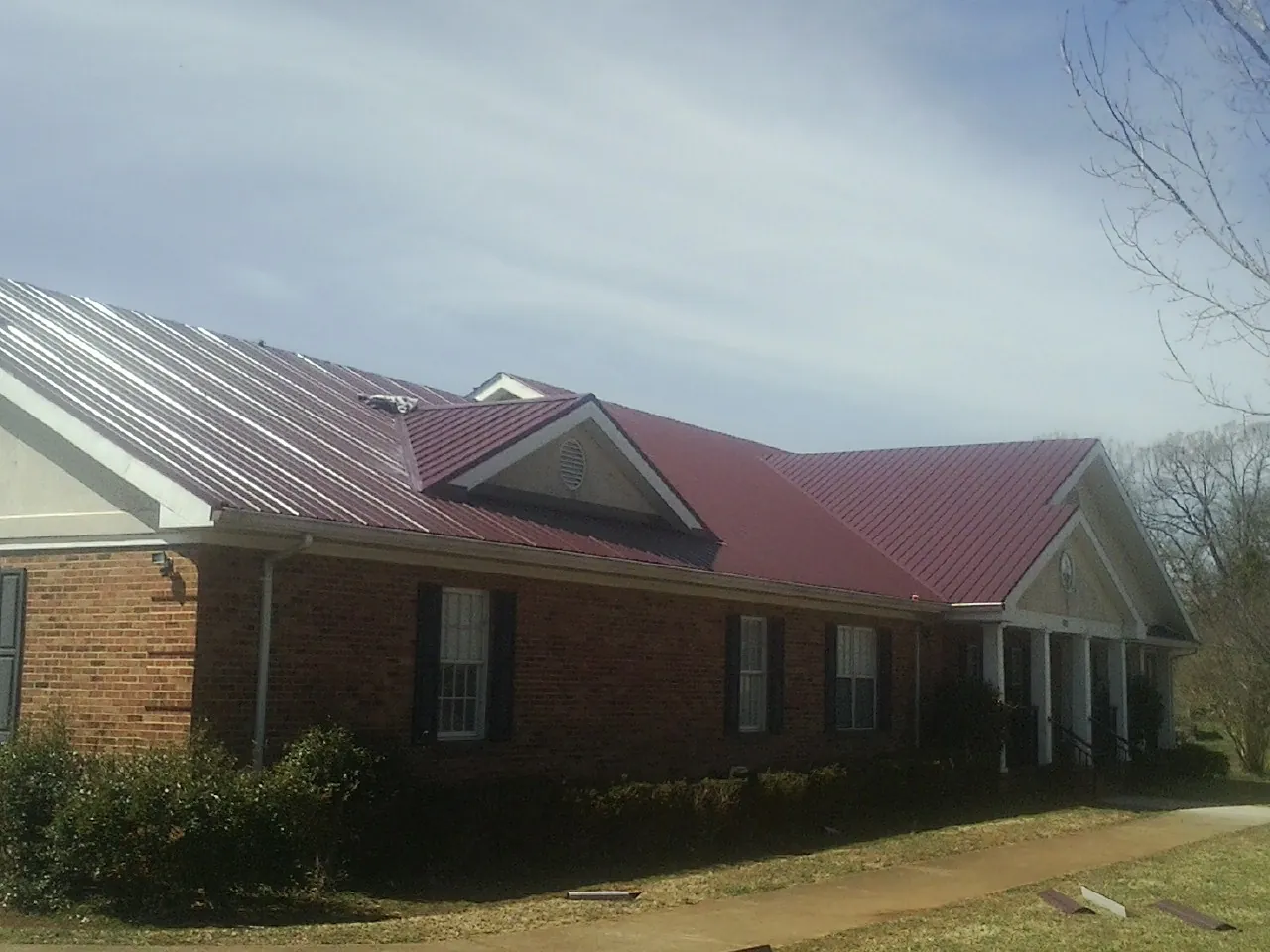 Red metal roof with gabled entries on a long brick building, from a Hail Damage Roof Repair job in Berwick